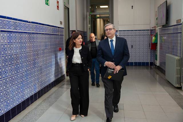 A man and a woman in business attire walking through a hallway with blue tiled walls.