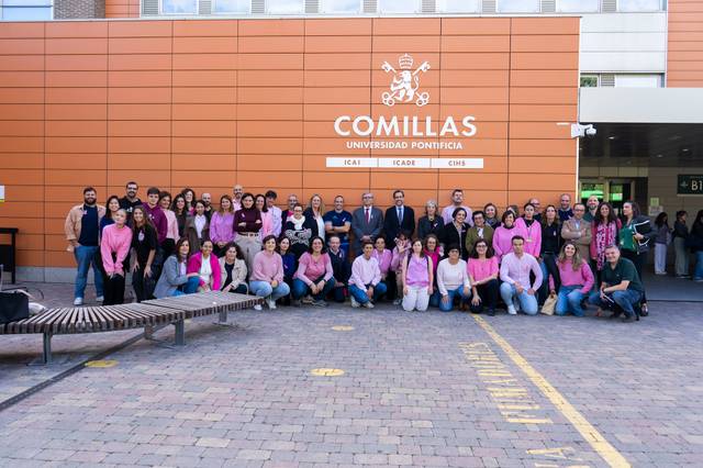 A group of people posing in front of the Comillas Pontifical University building.