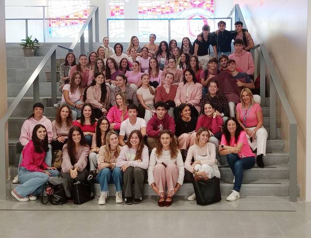 A large group of people wearing pink and white clothing sitting on steps inside a building.