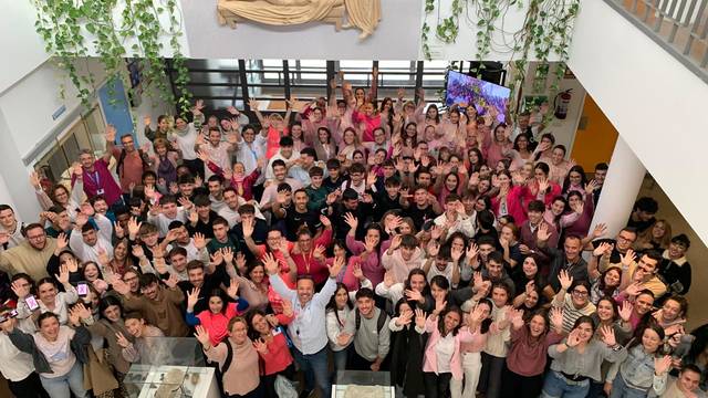 A large group of people smiling and waving at the camera in a spacious indoor area.