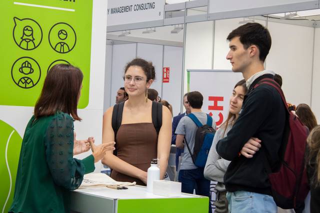 Young people engaging with a representative at a consulting firm booth during a career fair.