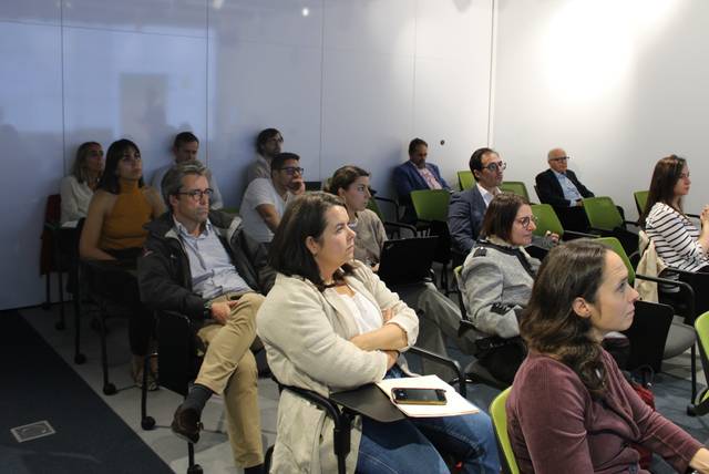 A group of adults sitting in chairs attentively listening in a conference room setting.