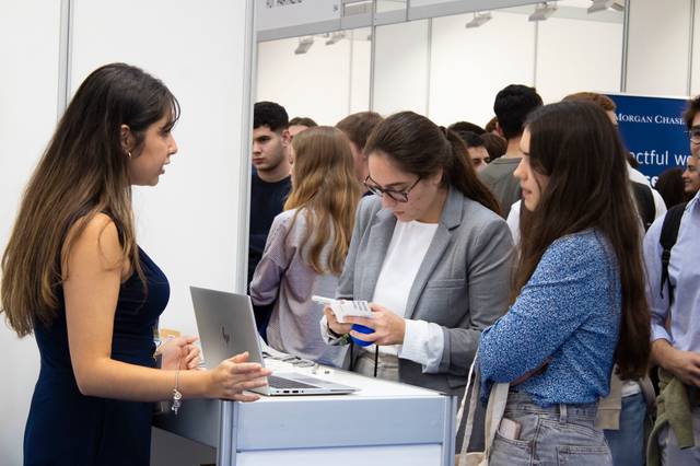 A group of people interacting at an exhibition booth with one person using a laptop.