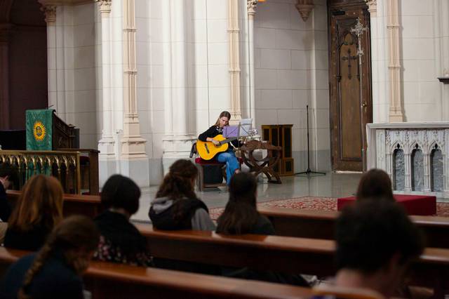 A person plays the guitar in front of an audience inside a church.