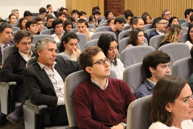 Grupo de personas jóvenes y adultas sentadas en un auditorio, escuchando atentamente una presentación o conferencia.