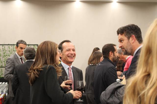 Un grupo de personas en un evento social interactuando alegremente mientras sostienen copas de vino.