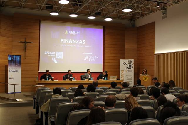 Una conferencia sobre finanzas con cuatro ponentes y una audiencia en un auditorio.