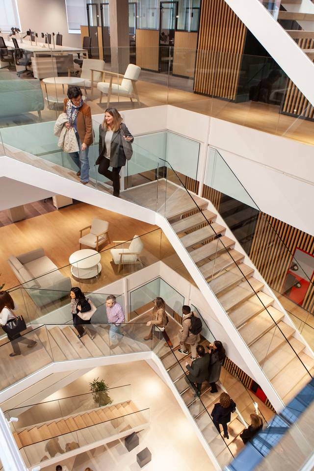 People walking and interacting in a modern multi-level office building with contemporary design elements.