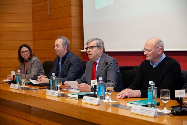 Cuatro personas están sentadas en una mesa durante una conferencia, con micrófonos y botellas de agua delante de ellos.