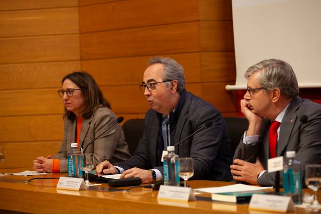 Tres profesionales sentados en una mesa durante un evento, hablando y escuchando en una conferencia.