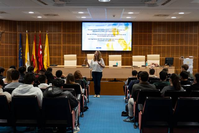 Una presentadora está dando una charla a un grupo de jóvenes sentados en un auditorio.