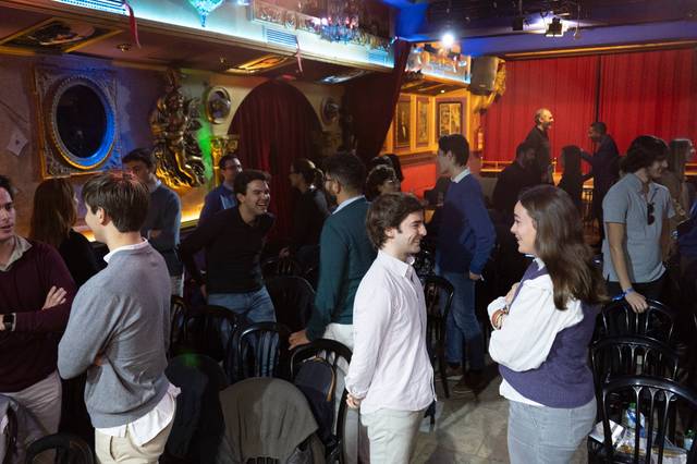 Personas conversando en un bar con decoración ecléctica y luces tenues.