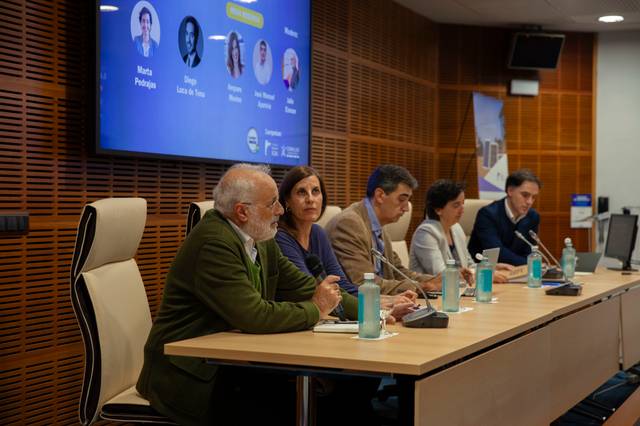 Personas sentadas en una mesa larga durante una conferencia en una sala moderna.