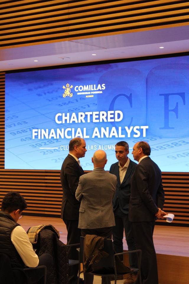 Varias personas conversan en un evento sobre análisis financiero en Comillas, con un fondo que muestra 'Chartered Financial Analyst'.