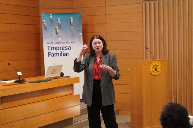 Una mujer está dando una conferencia en un auditorio con un cartel sobre 'Empresa Familiar' de fondo.