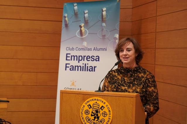 Una mujer dando un discurso en un podio con el escudo de la Universidad de Comillas y un cartel del Club Comillas Alumni Empresa Familiar de fondo.