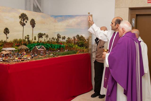 Sacerdotes realizando una bendición sobre un nacimiento detallado en un ambiente interior.