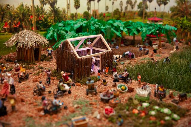 Una maqueta detallada de una escena rural con múltiples figuras de personas trabajando y estructuras, rodeada de vegetación.