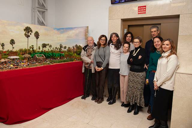 Grupo de personas posando junto a una exposición de maquetas en una sala.