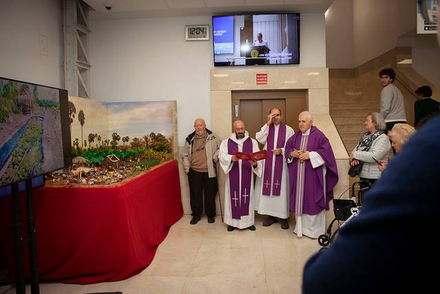 Tres sacerdotes vestidos con ropas litúrgicas moradas observan unas maquetas y pinturas en una exposición.