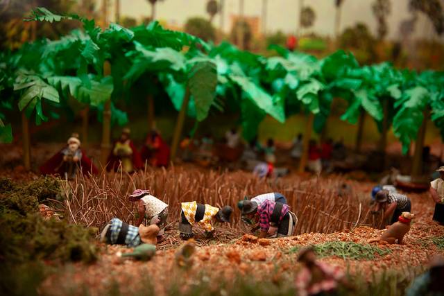 Una maqueta que representa a personas trabajando en un campo agrícola con árboles y plantas detalladas.