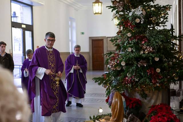 Sacerdotes caminando por un pasillo junto a un árbol de Navidad y un nacimiento.