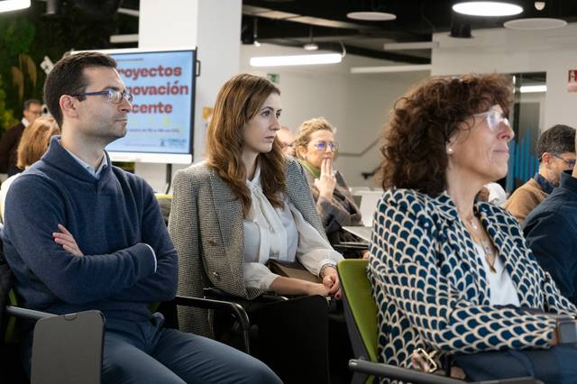 Grupo de personas adultas sentadas en sillas escuchando atentamente en una sala de conferencias.