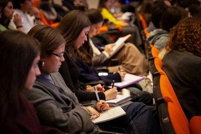 Estudiantes atentos tomando notas durante una conferencia en un auditorio.