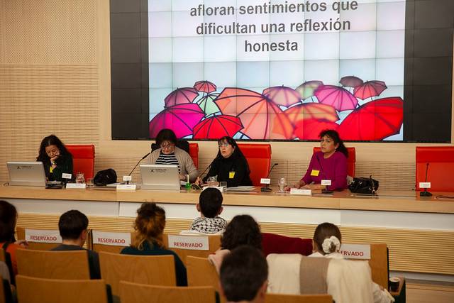 Cuatro personas participan en un panel de discusión en un auditorio con una gran pantalla mostrando un mensaje.