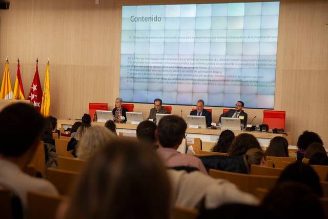 Imagen de un panel de discusión en un auditorio con público y una pantalla grande mostrando una presentación titulada 'Contenido'.