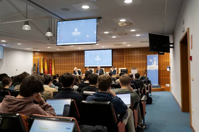 Un panel de discusión en un auditorio con estudiantes y ponentes sentados frente a una pantalla.