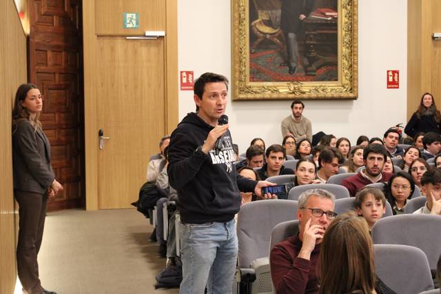 Una persona está hablando en un evento frente a una audiencia sentada.