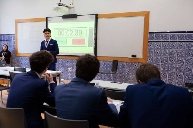Un grupo de jóvenes en un aula, mientras uno de ellos presenta frente a un cronómetro.