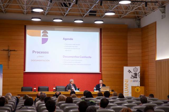 Una conferencia en un auditorio con dos ponentes y una presentación en la pantalla.