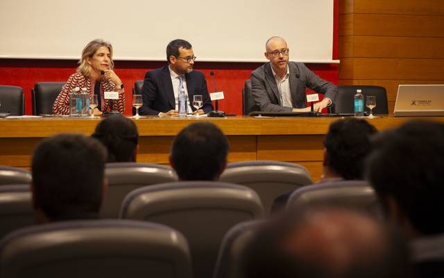 Una conferencia con tres ponentes delante de un público atento.