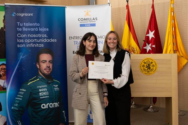 Entrega de un premio en un acto formal con banderas y un fondo promocional.