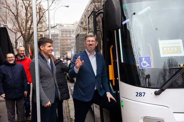 Un grupo de personas está junto a un autobús, con uno de los hombres saludando mientras otros observan.