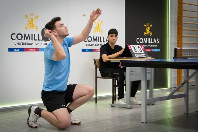 Un jugador de tenis de mesa se prepara para sacar mientras otro jugador lo observa.