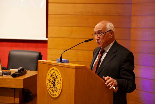 Un hombre mayor habla desde un atril en un evento académico.