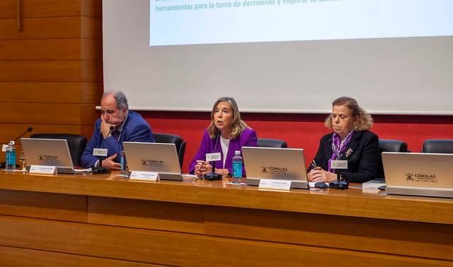 Una mesa redonda durante un evento, donde tres ponentes discuten temas relevantes frente a un público.