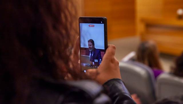 Una persona está grabando a un orador en un evento utilizando su teléfono móvil.