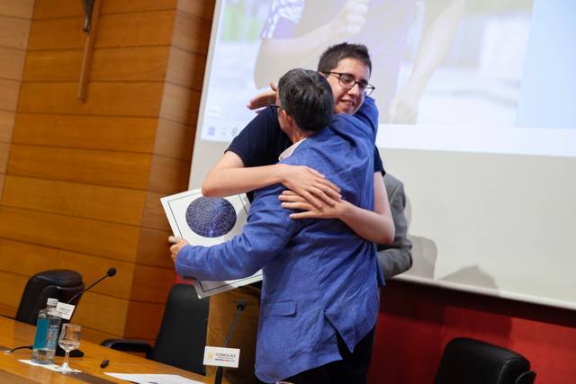 Dos personas se abrazan en un acto, mostrando un momento de celebración y emoción.