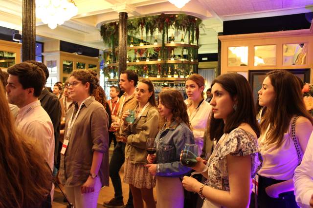 Una multitud de personas en un evento social disfrutando de bebidas en un ambiente decorado.