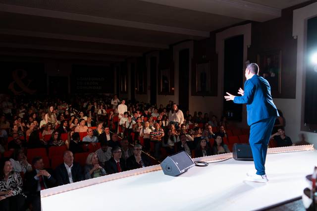 Un orador se presenta en un escenario frente a una audiencia numerosa.