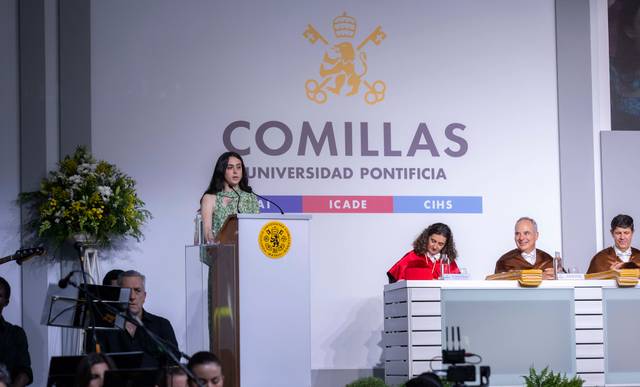 Una ceremonia en la Universidad Pontificia Comillas con una oradora en el podio y varias personas en el escenario.