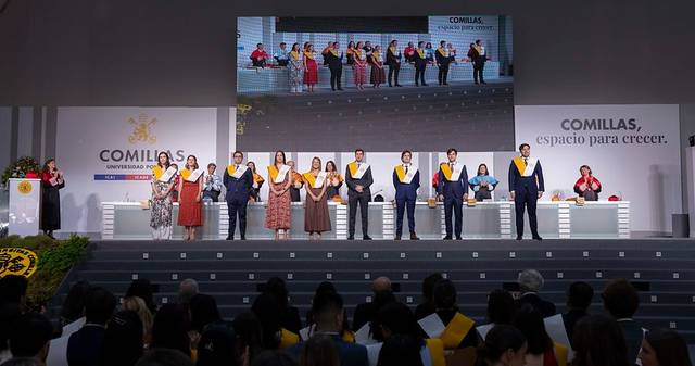 Graduación en la Universidad de Comillas con estudiantes vestidos formalmente en un escenario.