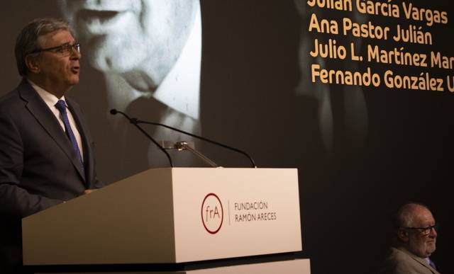 Un orador habla en un evento mientras una imagen en blanco y negro se proyecta en la pantalla de fondo.