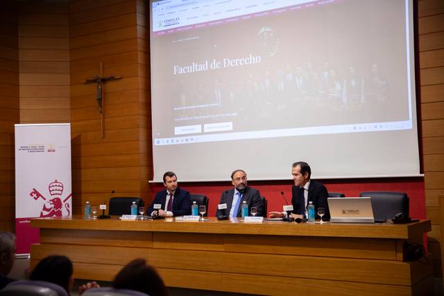 Imagen de una conferencia en la Facultad de Derecho con tres ponentes en el escenario.
