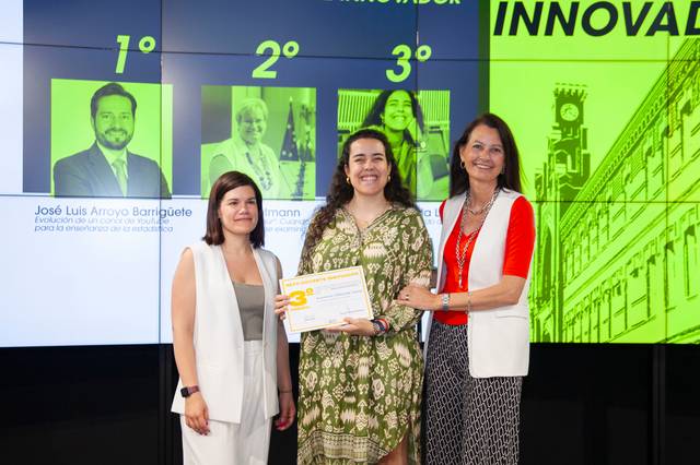 Una premiada sostiene un certificado junto a dos mujeres en un evento de reconocimiento.