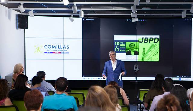 Un ponente presenta un evento en un aula moderna con una pantalla grande al fondo.